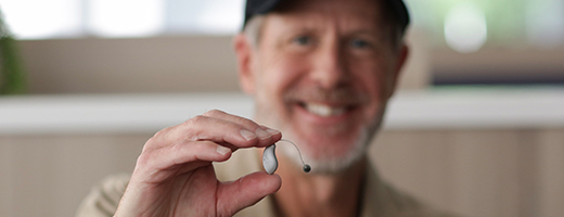 Image of a smiling veteran holding a hearing aid